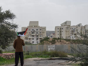 A Palestinian protester stands near the West Bank Barrier holding a flag as a form of protest in Bilin, West Bank, Palestine. (Shutterstock/ File Photo)