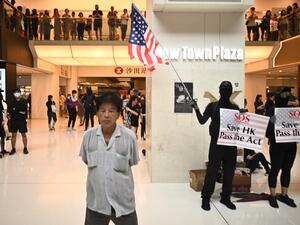 A man (L) walks past a person waving the US flag and holding a sign to rally for the US Congress to pass the Hong Kong Human Rights and Democracy Act, during a flash mob rally inside a shopping mall in the Sha Tin district in Hong Kong on October 13, 2019. (AFP/ File Photo)