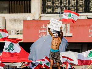 A topless Lebanese boy wearing body paint coloured with the Lebanese national flag and reading in Arabic "revolution" holds up a sign protesting against the ruling elites as others wave national flags during a demonstration on the sixth day of protest against tax increases and official corruption, at Nur Square in Lebanon's northern port city of Tripoli, on October 22, 2019. (AFP/ File Photo)