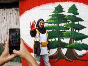 A woman shows her red-painted hand as she poses for a picture next to a mural depicting two cedars during a demonstration in southern city of Sidon on the seventh day of protest against tax increases and official corruption, on October 23, 2019. Mahmoud ZAYYAT / AFP