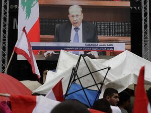 Lebanese people take cover from the rain under umbrellas as they watch a televised speech by President Michel Aoun, during a demonstration on the eighth day of protest against tax increases and official corruption, in Zouk Mosbeh, north of the capital Beirut, on October 24, 2019. The Lebanese president broke his silence after a week of unprecedented protests and expressed willingness to meet the demonstrators. JOSEPH EID / AFP
