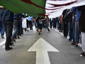 Algerian children run beneath a giant unfurled national flag carried by protesters marching during the 36th consecutive Friday anti-government demonstrations in the capital Algiers, on October 25, 2019. (RYAD KRAMDI / AFP)