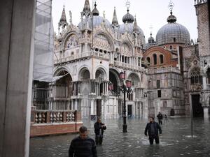 People wearing thigh boots cross flooded St. Mark's square by St. Mark's Basilica after an exceptional overnight "Alta Acqua" high tide water level Marco Bertorello / AFP