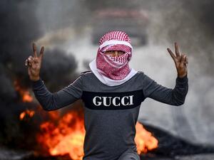 A masked Iraqi protester flashes the victory gesture as he stands before burning tires at a roadblock in the central holy shrine city of Najaf on November 18, 2019. (Haidar HAMDANI / AFP)