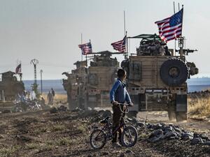 A Syrian boy on his bicycle looks at a convoy of US armoured vehicles patrolling fields near the northeastern town of Qahtaniyah at the border with Turkey (AFP)