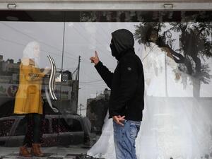 A masked member of the Palestinian Fatah political party tells a woman to close her shop in the southern West Bank city of Hebron after the party called a general strike over Israeli settlement activity in the area, on December 9, 2019. (AFP/ File Photo)