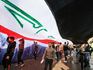 Protesters march with a giant Iraqi national flag during an anti-government demonstration in the capital Baghdad's central Tahrir Square on December 22, 2019.  SABAH ARAR / AFP