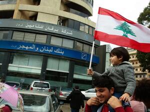 A Lebanese protester carries a child as he takes part in a rally in front of a bank in the southern city of Sidon (Saida) on December 30, 2019 to protest against nationwide imposed restrictions on dollar withdrawals and transfers abroad in an attempt to conserve dwindling foreign currency reserves. (AFP/ File Photo)