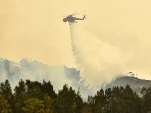 A helicopter drops water on a bushfire outside of Batemans Bay in New South Wales on January 2, 2020. Australia authorised the forced evacuation of residents on January 2 amid a mass exodus of tourists from fire-ravaged coastal communities, as the country braces for a weekend heatwave expected to fan deadly bushfires. PETER PARKS / AFP