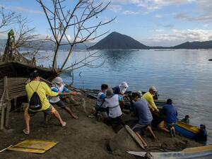A group of fishermen haul a boat from the water as they make repairs to their operations affected by the eruption of the Taal volcano, in Buso Buso on January 20, 2020. Ed JONES / AFP