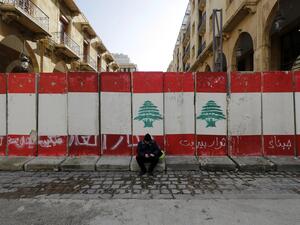 A man sits in front of a wall of cement blocks, set up by Lebanese security forces to bar a street leading to the country's parliament building in the capital Beirut's downtown district, on January 24, 2020. JOSEPH EID / AFP