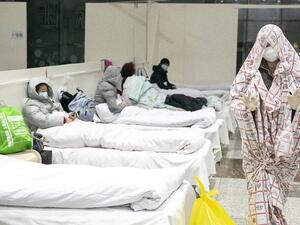 This photo taken on February 5, 2020 shows a patient (R) covered with a bed sheet at an exhibition centre converted into a hospital as it starts to accept patients displaying mild symptoms of the novel coronavirus in Wuhan in China's central Hubei province. China scrambled to find bed space for thousands of newly infected patients on February 6, as the toll from a deadly new virus jumped again with more than 28,000 people known infected nationwide and 563 deaths. STR / AFP