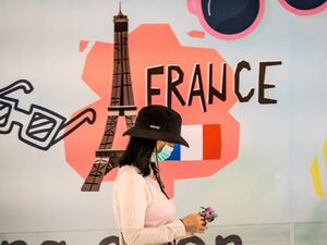 A woman, wearing a protective facemask amid fears over the spread of the COVID-19 coronavirus, walks in front of an advertisement board in Bangkok on February 17, 2020 featuring the Eiffel tower in France. Mladen ANTONOV / AFP