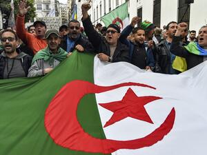 People chant slogans as they wave a large Algerian national flag during a weekly anti-government demonstration in the capital Algiers on March 6, 2020. Protests against cronyism have continued in Algeria despite former president Abdelaziz Bouteflika's resignation and the election of a new president in December 2019. RYAD KRAMDI / AFP