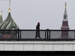 A man walks along a bridge over the Moskva river in front of St. Basil's Cathedral and the Kremlin in downtown Moscow on March 13, 2020. Yuri KADOBNOV / AFP