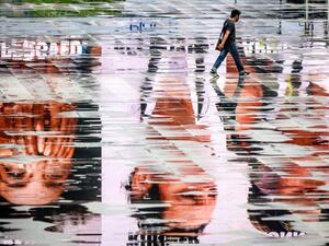 A man wearing a facemask, amid concerns over the spread of the COVID-19 coronavirus, walks among puddles reflecting advertisement screens on an empty square in Bangkok on March 15, 2020. Mladen ANTONOV / AFP