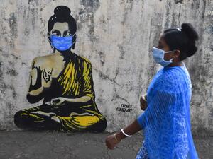 A resident wearing a facemask amid concerns over the spread of the COVID-19 novel coronavirus walks past a graffiti of Buddha wearing facemask, in Mumbai on March 16, 2020. INDRANIL MUKHERJEE / AFP