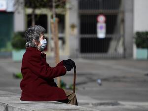 In this file photo taken on March 08, 2020 an elderly woman wearing a protective face mask sits on a bench in the city centre of Milan, after millions of people were placed under forced quarantine in northern Italy as the government approved drastic measures in an attempt to halt the spread of the COVID-19 outbreak, caused by the novel coronavirus that is sweeping the globe. While Italy is a country of senior citizens, the oldest in Europe according to statistics, and few of them live in retirement homes, t
