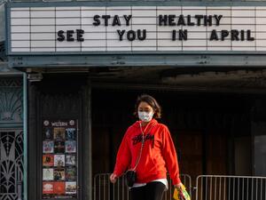 A woman walks wearing a mask to protect herself from the novel coronavirus (COVID-19) in front of a closed theater in Koreatown, Los Angeles, on March 21, 2020. All 40 million residents of California were on March 19 ordered to stay at home indefinitely in a bid to battle the coronavirus pandemic in the nation's most populous state. Apu GOMES / AFP