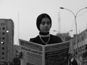 A hunt for the right moment. A young woman reads a newspaper near Tahrir Square in Baghdad during protests. (Amir Hazim)