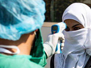A health care worker checks the temperature of a woman arriving by bus to Syrian Kurdistan (Rojava) from the Kurdistan Region to test for the coronavirus, Feb. 26, 2020 (Photo: AFP/Delil Souleiman)