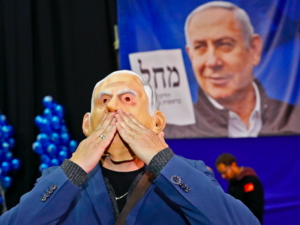 A man wearing a "Benjamin Netanyahu" face mask blows kisses as he stands before a giant Likud party election poster showing the face of its leader Prime Minister Netanyahu at the Likud's electoral headquarters in the coastal city of Tel Aviv on March 2, 2020, after polls officially closed. Exit polls by three Israeli television networks, released after polls closed, gave Likud between 36 and 37 seats in Israel's 120-member parliament against Blue and White's estimated 32 or 33. Jack GUEZ / AFP