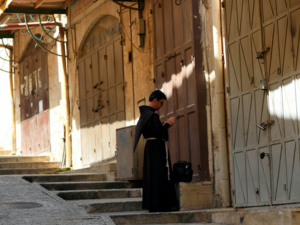 A Fransiscan friar checks his mobile phone in front of closed shops, in the Old City of Jerusalem on March 16, 2020, after Israel imposed tight restrictions to contain the COVID-19 coronavirus disease. In the millenary alleys of Jerusalem's Old City where a crowd of visitors usually walks the alleys, the sellers of ceramics, T-shirts and rugs have no one left to woo. Emmanuel DUNAND / AFP