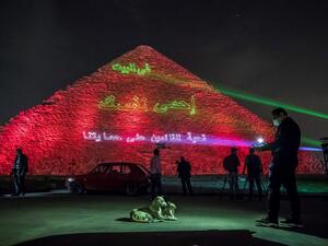 A man takes pictures of dogs in front of the Great pyramid of Kheops at the Giza plateau outside the Egyptian capital Cairo where a laser projection writes "Stay at home, stay safe. Thanks to those keeping us safe" on March 30, 2020, amid the spread of the COVID-19 infection, caused by the novel coronavirus. Khaled DESOUKI / AFP