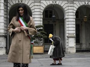 Turin mayor Chiara Appendino (L) stands at attention as an elderly woman walks past during a minute of silence at noon on March 31, 2020 in Turin as flags are being flown at half-mast in cities across Italy to commemorate the victims of the virus, during the country's lockdown aimed at curbing the spread of the COVID-19 infection, caused by the novel coronavirus. Marco BERTORELLO / AFP