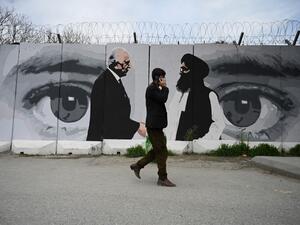 A man wearing a facemask as a precautionary measure against the COVID-19 novel coronavirus walk past a wall painted with images of US Special Representative for Afghanistan Reconciliation Zalmay Khalilzad (L) and Taliban co-founder Mullah Abdul Ghani Baradar (R), in Kabul April 5, 2020. WAKIL KOHSAR / AFP
