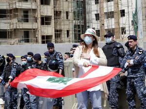 An anti-government protester waves the national flag as security forces wearing masks stand guard during a convoy protest in front of Mohammad Al-Amin mosque in the Lebanese capital Beirut on April 22, 2020, amid an economic crisis exacerbated by the coronavirus pandemic. (AFP/File)