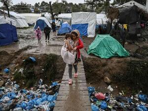 A woman carries her child as she crosses a wooden bridge in the refugee camp of Moria, on the island of Lesbos, November 26. (AFP)