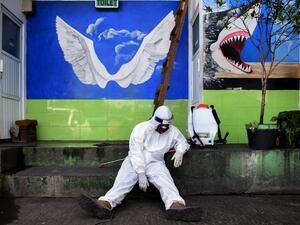A health agency official, seen alongside his disinfectant dispenser, rests by the entrance to a public toilet as other colleagues (not pictured) conduct polymerase chain reaction (PCR) testing for the COVID-19 coronavirus at a bus station in Bandung, West Java, on May 13, 2020. TIMUR MATAHARI / AFP