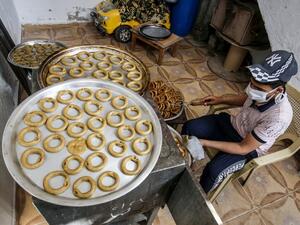 A Palestinian man, wearing protective face masks and gloves during the COVID-19 pandemic, bakes traditional cookies in preparation for the upcoming Eid al-Fitr holiday which marks the end of the Islamic holy month of Ramadan, in the southern Gaza Strip city of Rafah on May 17, 2020. SAID KHATIB / AFP