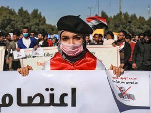 In this file photo taken on February 2, 2020, An Iraqi student wearing a beret and a surgical mask holds signs with a red X mark on the face of the new Iraqi prime minister designate Mohammad Allawi reading in Arabic "rejected by order of the people" during a demonstration against him in the central holy shrine city of Karbala. (AFP)
