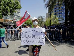 A Lebanese protester wearing a protective mask amid the COVID-19 pandemic, lifts a placard which reads "the October 17 revolution is against figures of crime and corruption. The resistance is our pride", as he demonstrates in the capital Beirut, on May 30, 2020. In parallel, anti-government protesters demonstrated on the same day demanding the implementation of United Nations resolutions including the disarmament of armed groups in the country. ANWAR AMRO / AFP