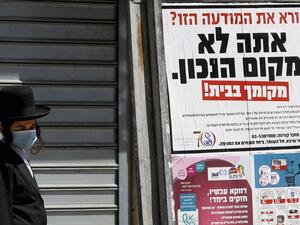 An ultra-Orthodox Jewish man wearing a mask walks past a sign reading in Hebrew "Reading this ad? You're not in the right place. (AFP/File Photo)