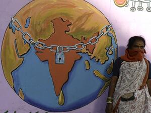 A labourer with her face covered waits for a local transport beside a graffiti depicting a world under lockdown, during a nationwide lockdown as a preventive measure against the COVID-19 coronavirus, on the outskirts of Hyderabad on May 29, 2020. NOAH SEELAM / AFP