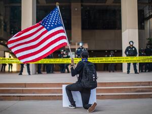 A demonstrator holding a US flag kneels in front of the Police at the Anaheim City Hall on June 1, 2020 in Anaheim, California, during a peaceful protest over the death of George Floyd. (Apu GOMES / AFP)