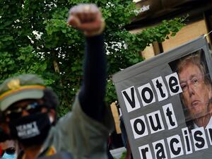 A demonstrator raises his fist in front of a sign calling to vote out racism with a picture of President Donald Trump during a peaceful protest against police brutality and the death of George Floyd, on June 7, 2020 in Washington, DC. Olivier DOULIERY / AFP