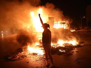 A Lebanese anti-government protester raises her clenched fist as tires burn behind her during a demonstration against dire economic conditions in the downtown districtof the capital Beirut, late on June 11, 2020. The Lebanese pound sank to a record low on the black market on June 11 despite the authorities' attempts to halt the plunge of the crisis-hit country's currency, money changers said. Lebanon is in the grips of its worst economic turmoil in decades, and holding talks with the International Monetary 