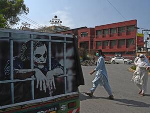 People wearing facemasks cross a street beside an auto-rickshaw with a graffiti depicting actor Heath Ledger (L) in his role as the Joker, in Rawalpindi on June 26, 2020.  Aamir QURESHI / AFP