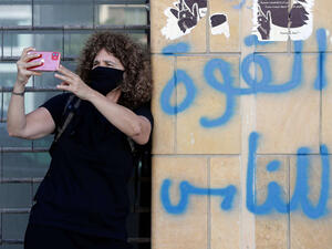 Lebanese director Carol Mansour uses her phone to film while wearing a face mask and standing by graffiti reading in Arabic “power to the people”, in the centre of the capital Beirut. (AFP)