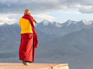 Monk lama in red and yellow color clothing standing in front of mountains (Shutterstock)	 