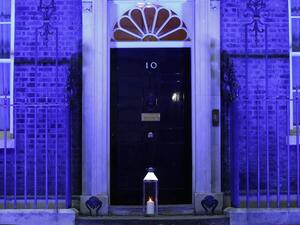 A candle is lit and placed on the doorstep of 10 Downing Street in central London on July 4, 2020 in honour of the tens of thousands of people who have died as a result of the coronavirus pandemic in the UK as the building itself is lit up blue as a tribute to NHS workers and to mark the 72nd anniversary of the NHS. Tolga AKMEN / AFP