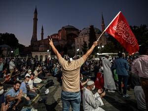 A man flashes the V for Victory hand sign and waves a flag outside the Hagia Sophia museum in Istanbul on July 10, 2020 as people gather to celebrate after a top Turkish court revoked the sixth-century Hagia Sophia's status as a museum, clearing the way for it to be turned back into a mosque. Ozan KOSE / AFP