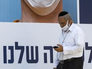 A mask-clad man browses his phone as he walks past a billboard showing other mask-clad faces and adequate social distance measures, raising awareness about COVID-19 coronavirus pandemic precautions, in the centre of the Israeli city of Ramat Gan, east of Tel Aviv, on July 17, 2020. Israel's government said it was imposing new restrictions to limit the spiraling spread of coronavirus in the hope of avoiding a general lockdown further along the line. It said that from 5:00pm local time (1400 GMT) on Friday un