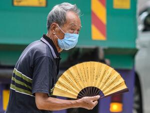 A man uses a traditional Chinese fan as he walks across a main road in Hong Kong on July 20, 2020. ANTHONY WALLACE / AFP