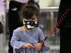A girl wearing a protective mask and a child safety leash waits with members of her family to board a flight at the departure hall of Baghdad international airport following its reopening on July 23, 2020, after a closure forced by the coronavirus pandemic restrictions aimed at preventing the spread of the deadly COVID-19 illness in Iraq. AHMAD AL-RUBAYE / AFP