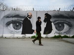 A man wearing a facemask against coronavirus walks past a wall painted with images of US Special Representative for Afghanistan Reconciliation Zalmay Khalilzad and Taliban co-founder Mullah Abdul Ghani Baradar, in Kabu'. AFP | WAKIL KOHSAR